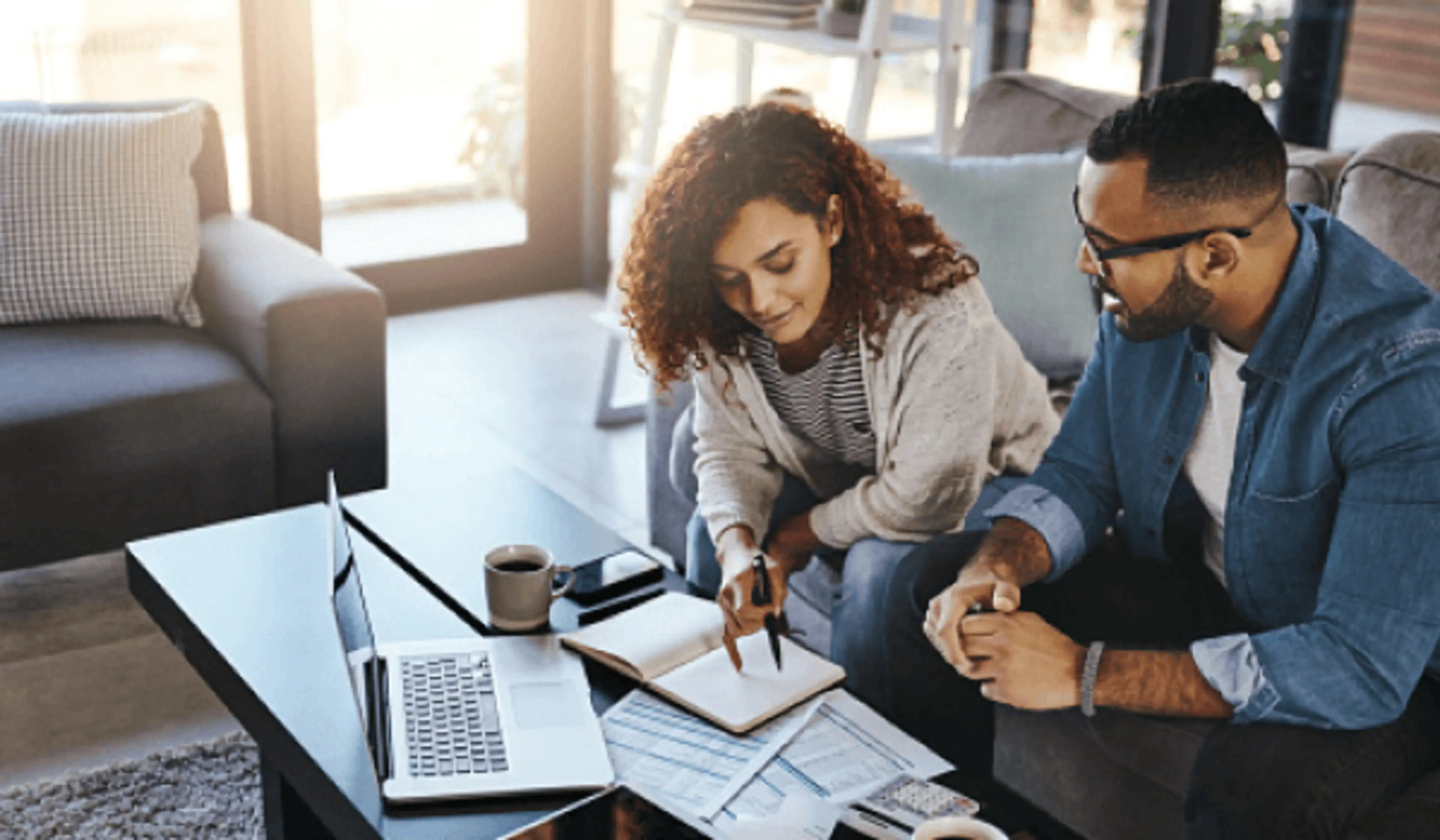 A man and woman go over their finances at the coffee table to decide if they should get a joint bank account.