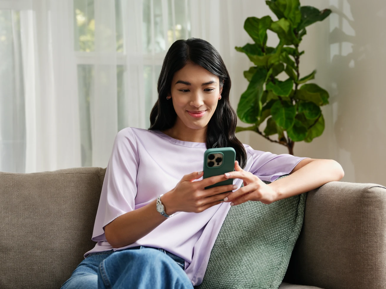 A woman sitting on the couch, smiling while using her phone to file taxes. 