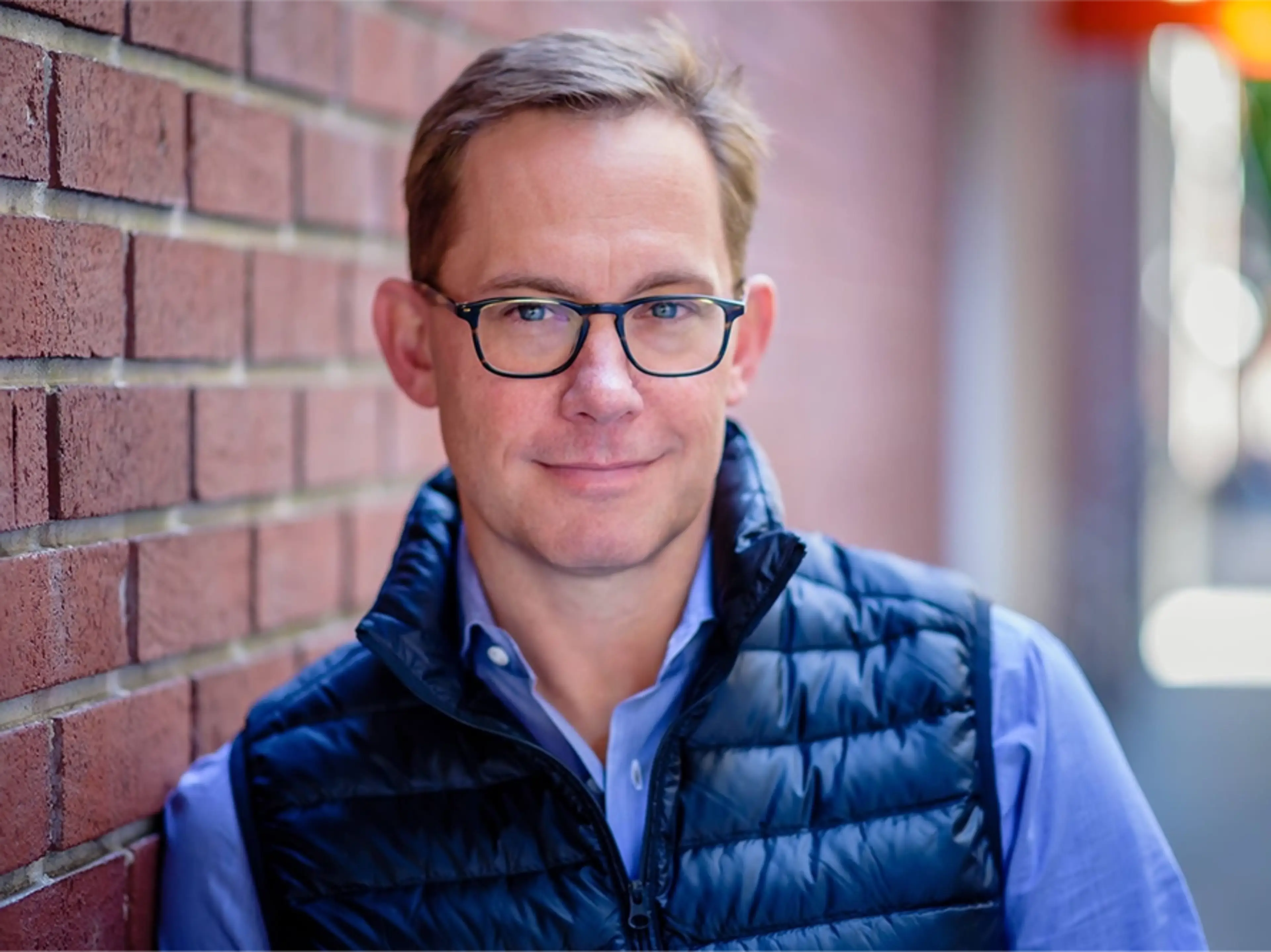 Chris Britt, Chime CEO smiling and leaning against a brick wall.