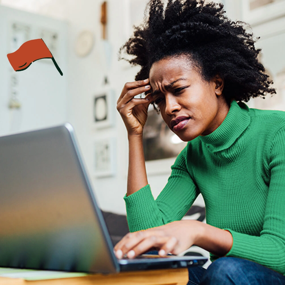 Person in green sweater looking stressed while working on laptop, with a red flag icon in the corner.