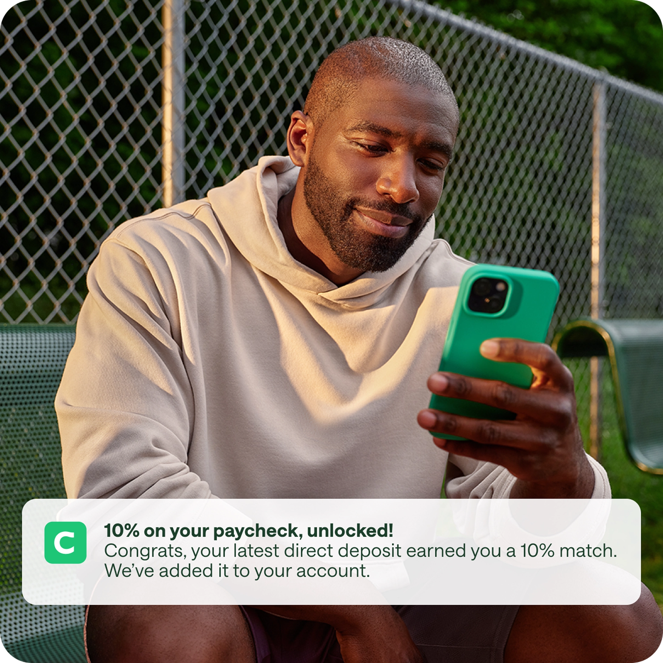 A man smiling and looking at his green cell phone. A mobile pop-up alert reads: 10% on your paycheck, unlocked! Congrats, your latest direct deposit earned you 10% match. We've added it to your account.