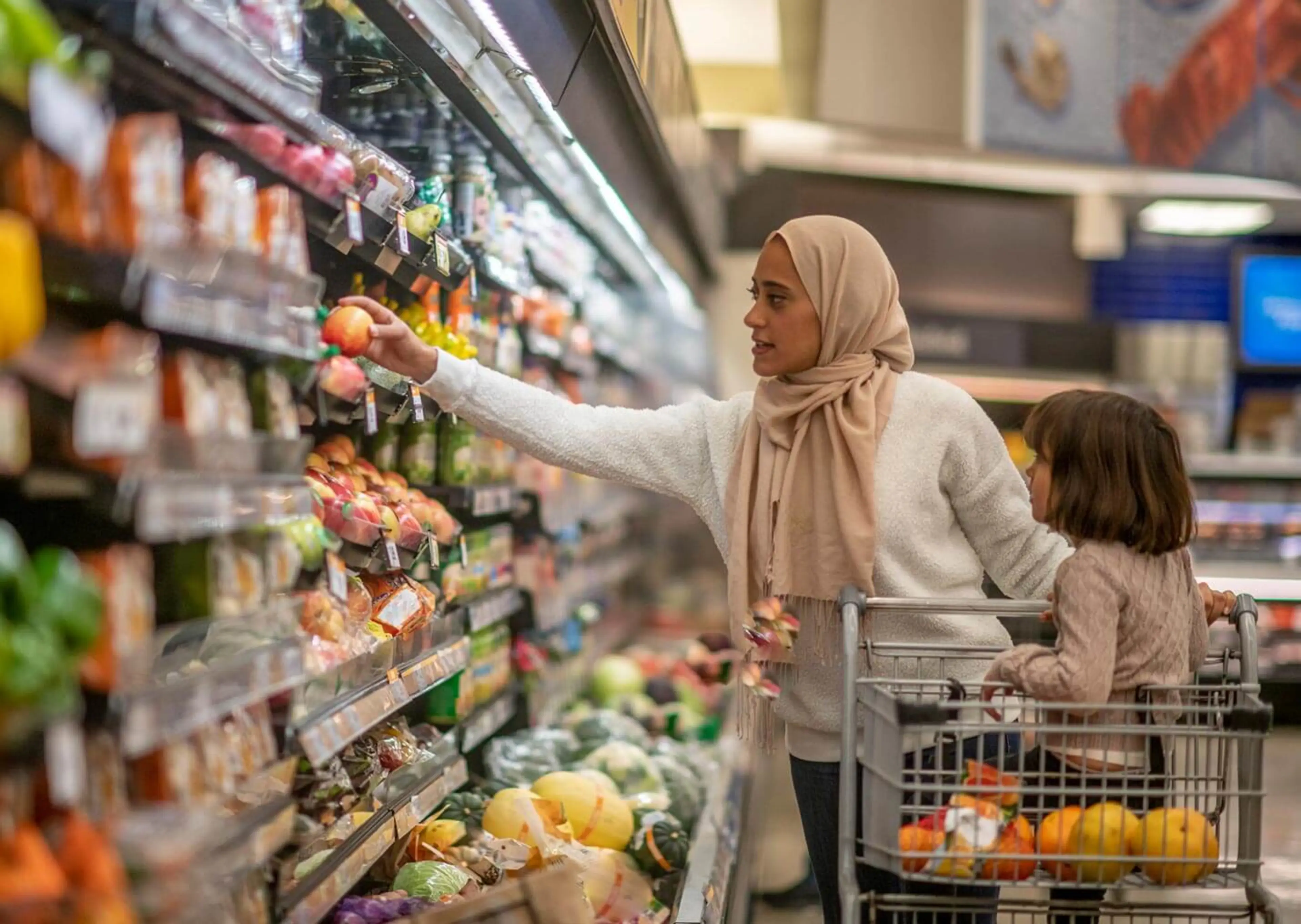 A woman shopping in a grocery store pulls an item from the shelf.