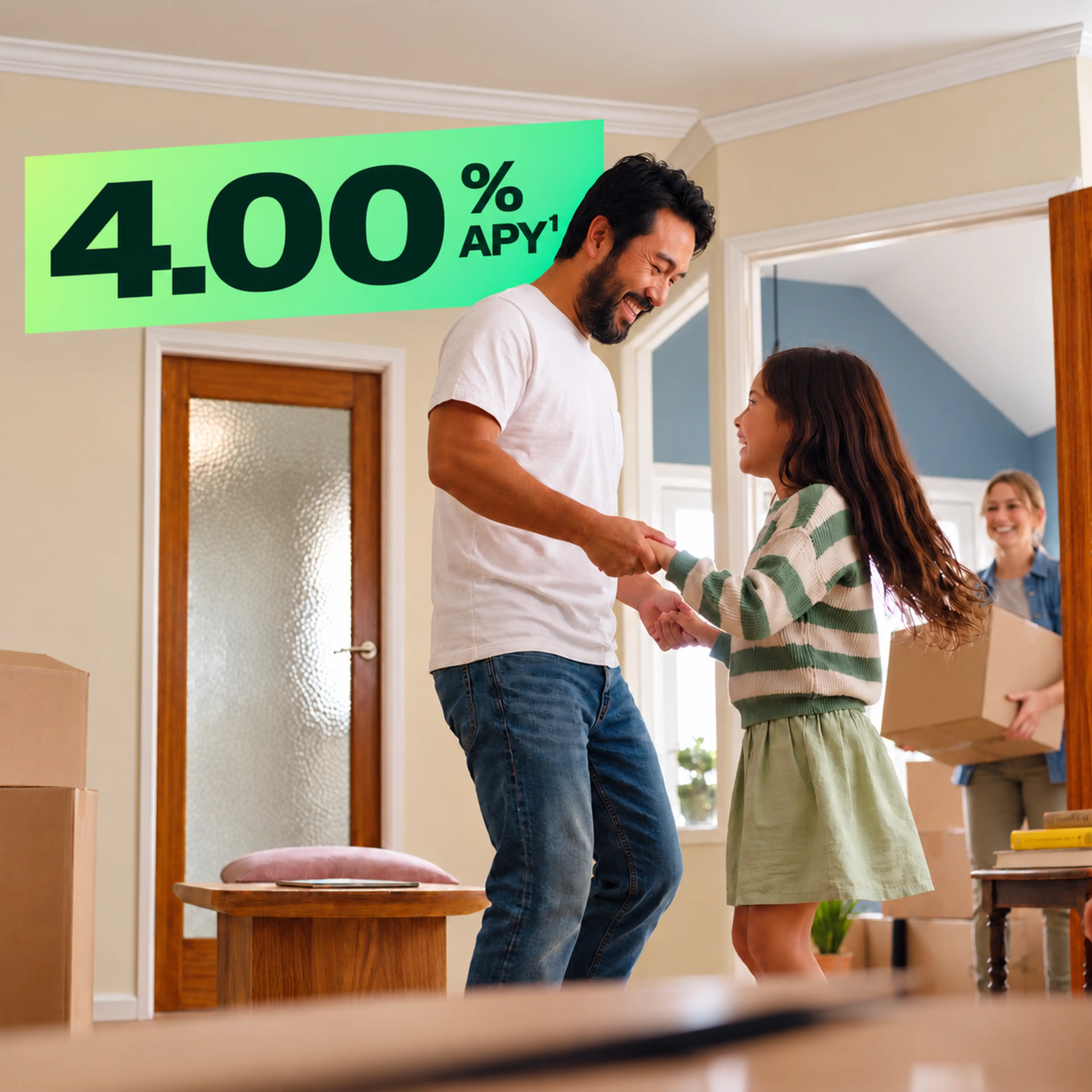 A smiling father in a white t-shirt and jeans dances with his young daughter in a bright, cozy home.