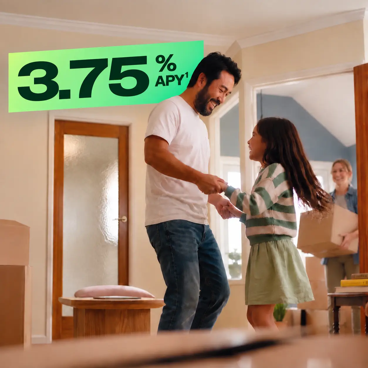 A smiling father in a white t-shirt and jeans dances with his young daughter in a bright, cozy home.