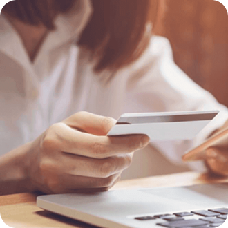 Person in white shirt holding a credit card while seated at a desk with a laptop visible.