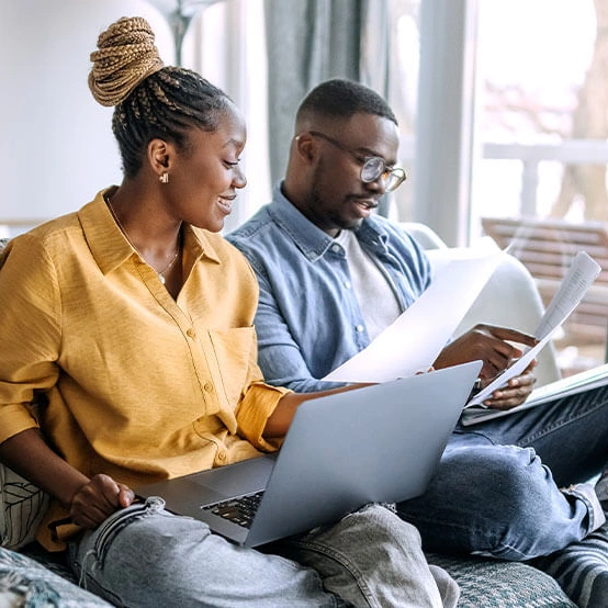 A couple sits together in their living room reviewing financial paperwork and researching the question, “what is a high-yield savings account?”