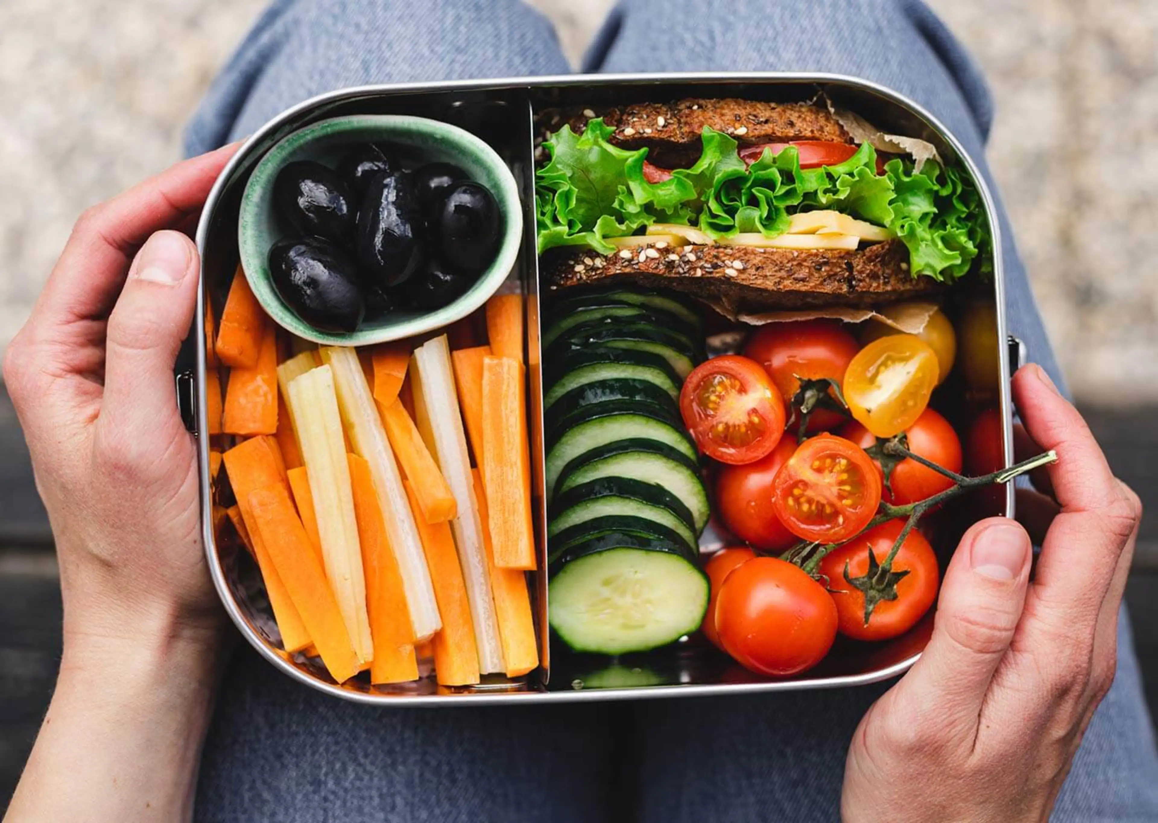 A closeup shot captures a person holding a packed lunch, alluding to some popular money saving hacks.