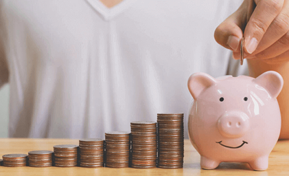 Person in white shirt placing coin into pink piggy bank beside ascending stacks of coins showing savings growth.