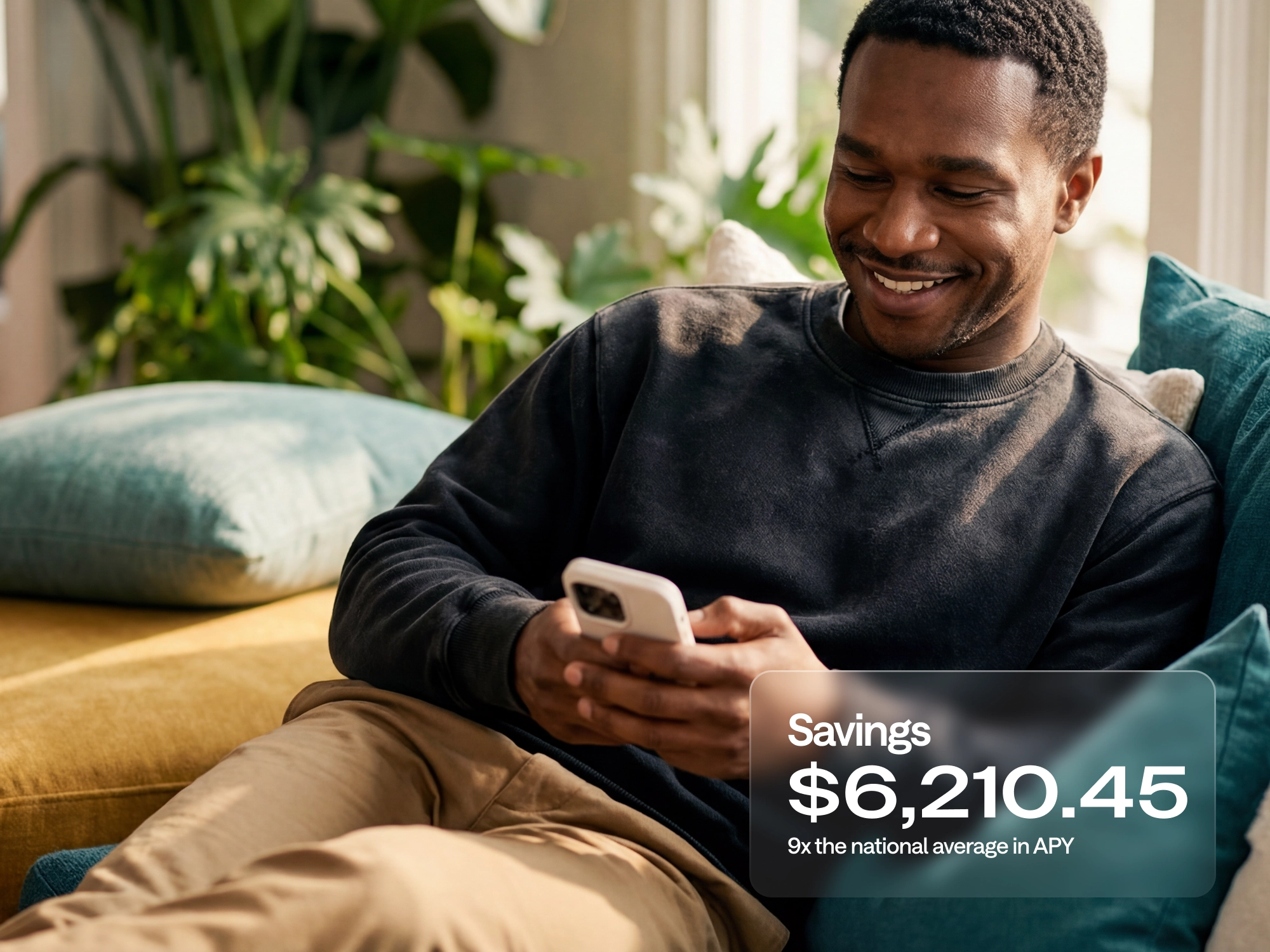 A smiling man on a couch checks his phone, with a savings balance of $6,210.45 shown, 9x the national average APY.