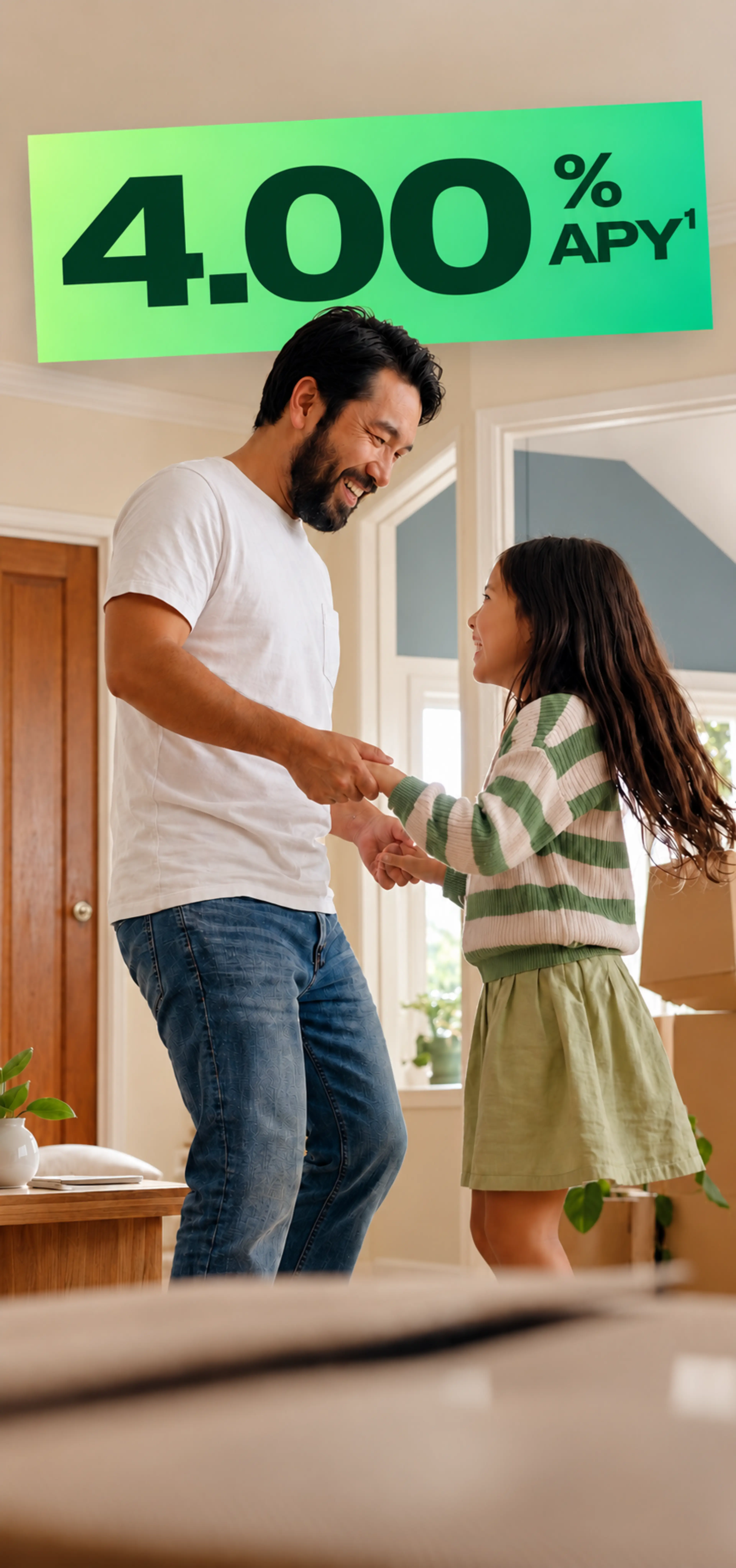 A smiling father in a white t-shirt and jeans dances with his young daughter in a bright, cozy home.