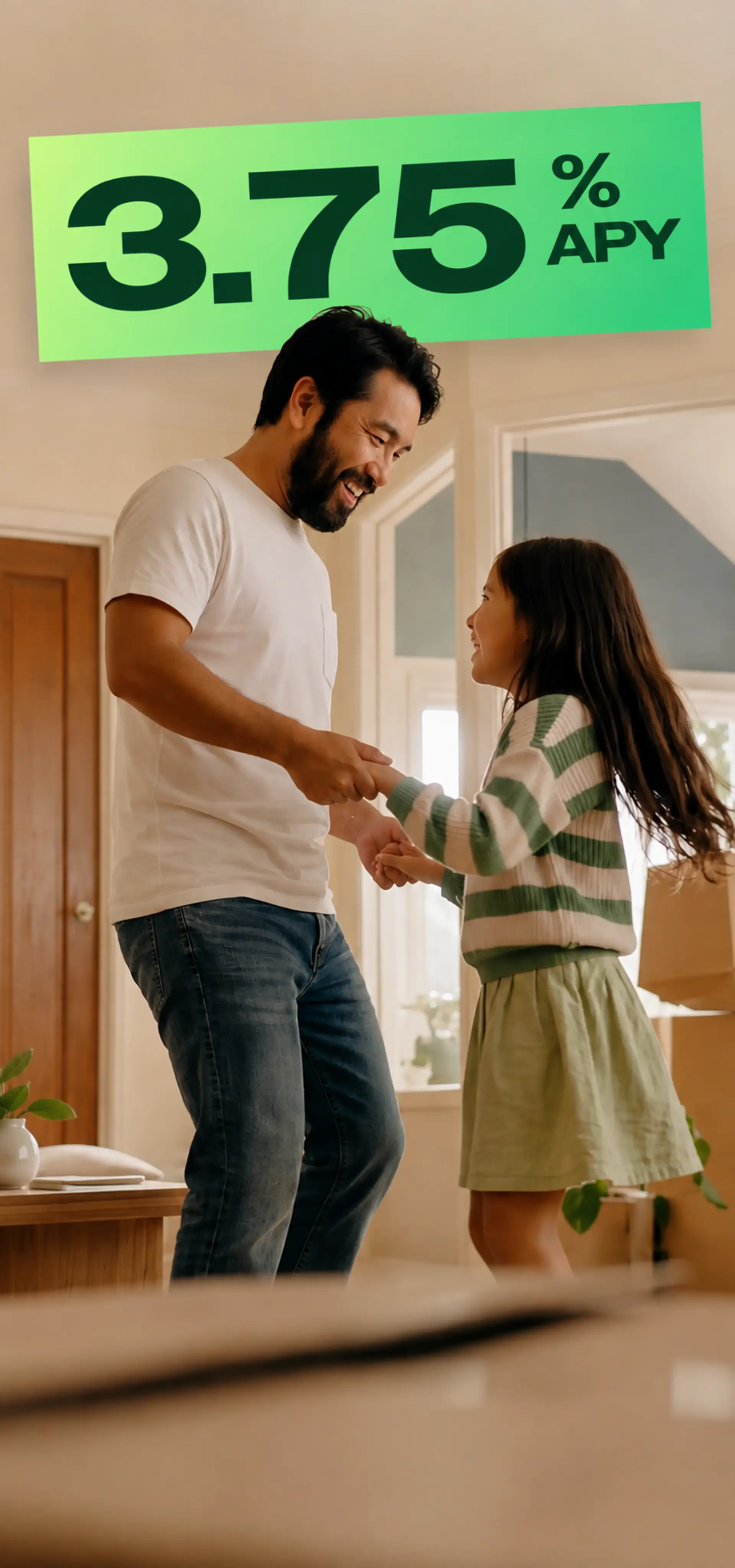 A smiling father in a white t-shirt and jeans dances with his young daughter in a bright, cozy home.