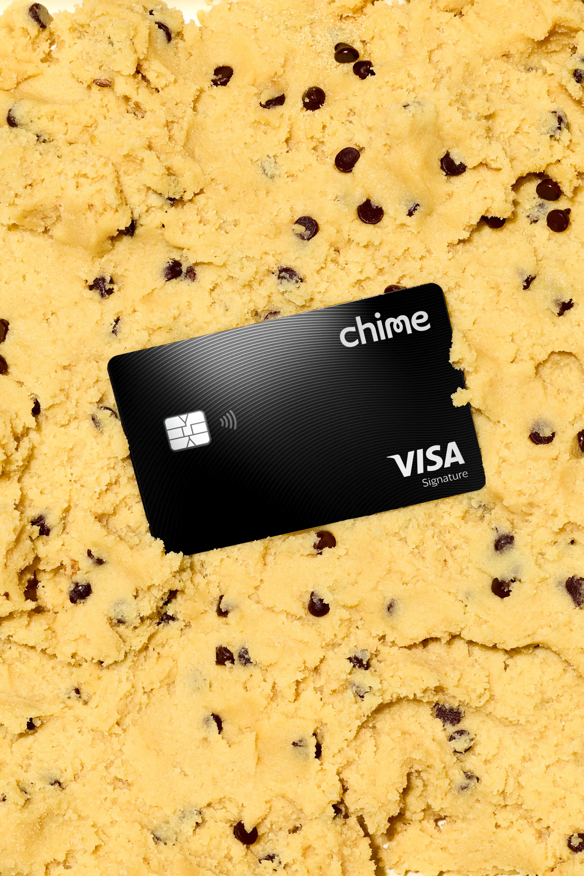 A black Chime Visa Signature card resting on a bed of yellow chocolate chip cookie dough.