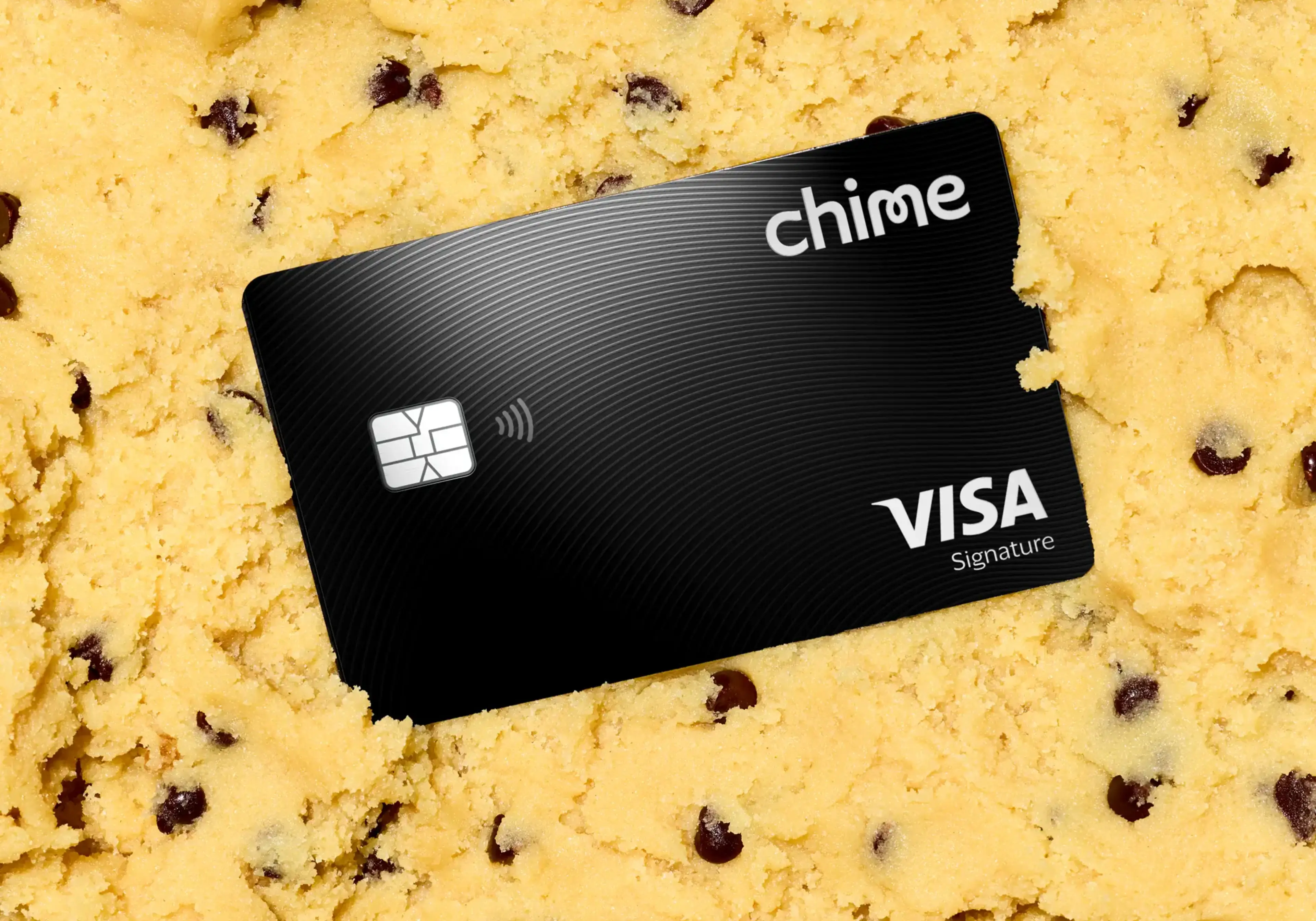 A black Chime Visa Signature card resting on a bed of yellow chocolate chip cookie dough.