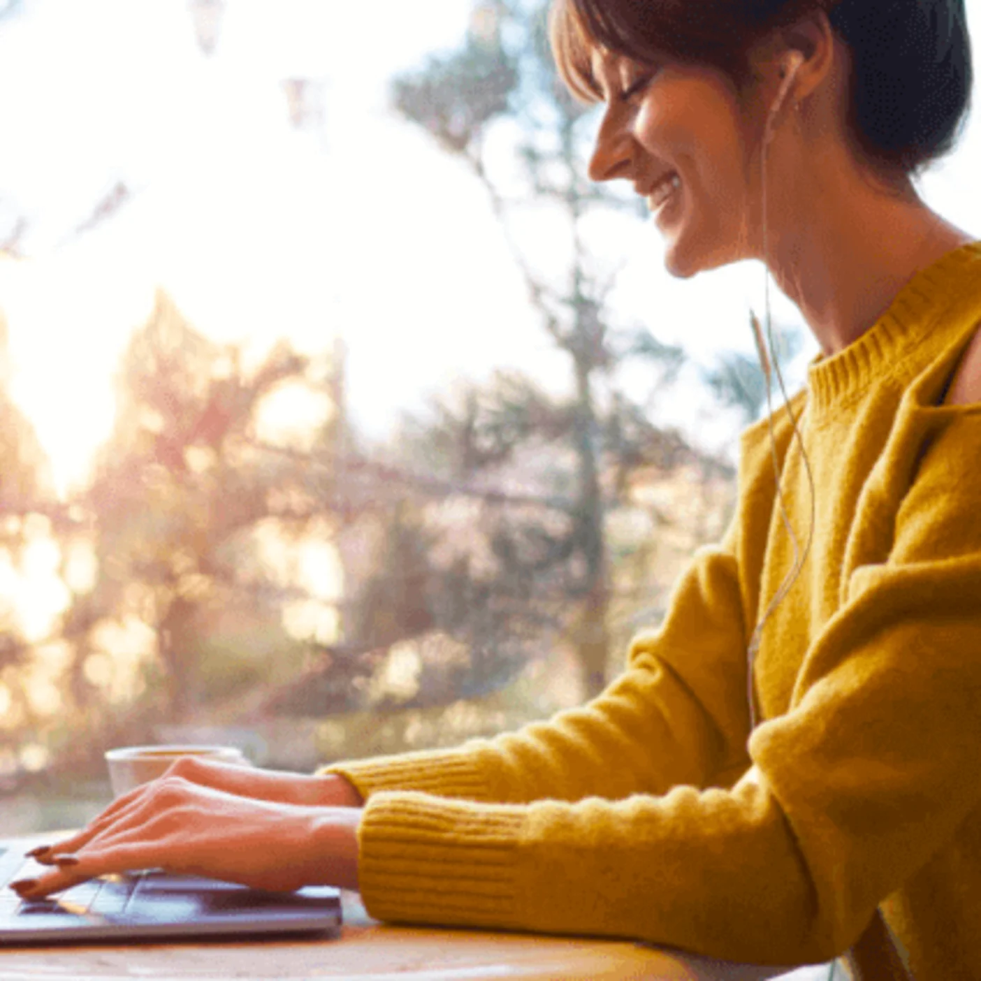 Woman sitting down at a desk with the sunrise in the background. She is typing on a computer and smiling.
