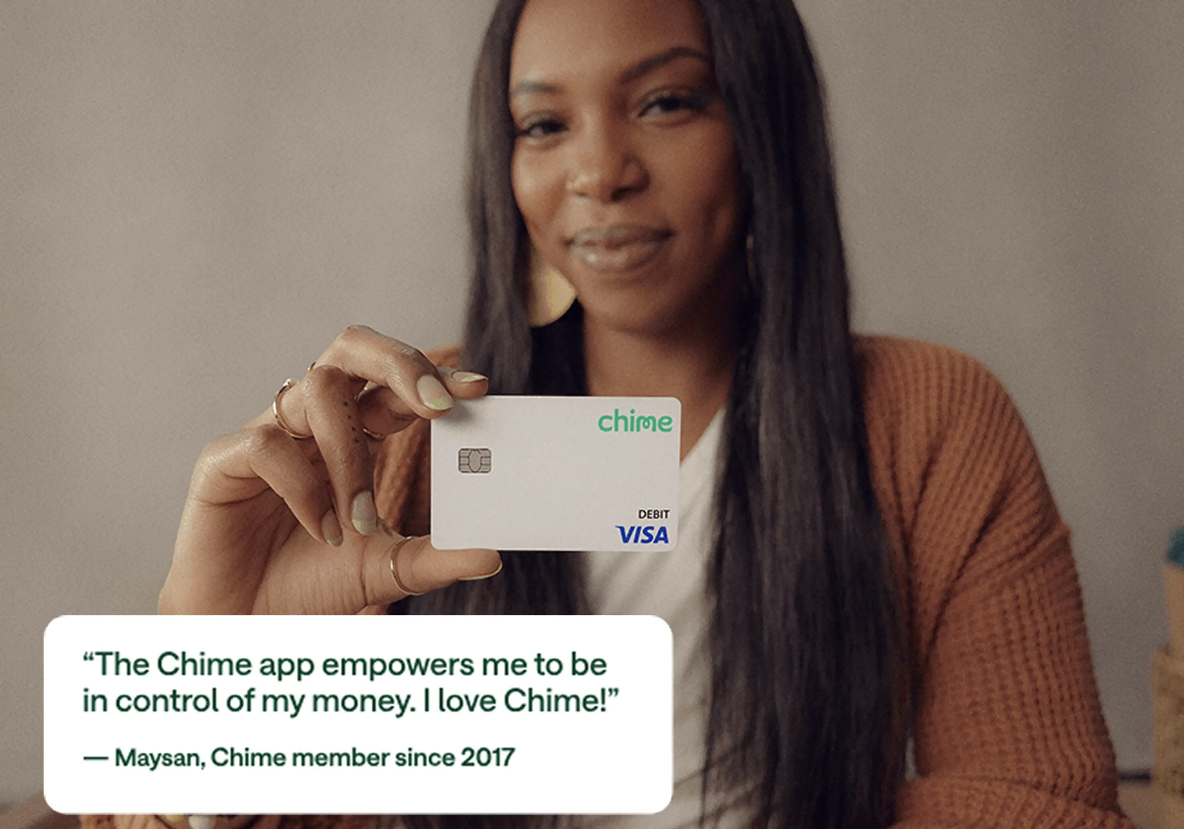 Person in orange cardigan holding a white Chime debit card with testimonial quote from Maysan, member since 2017.