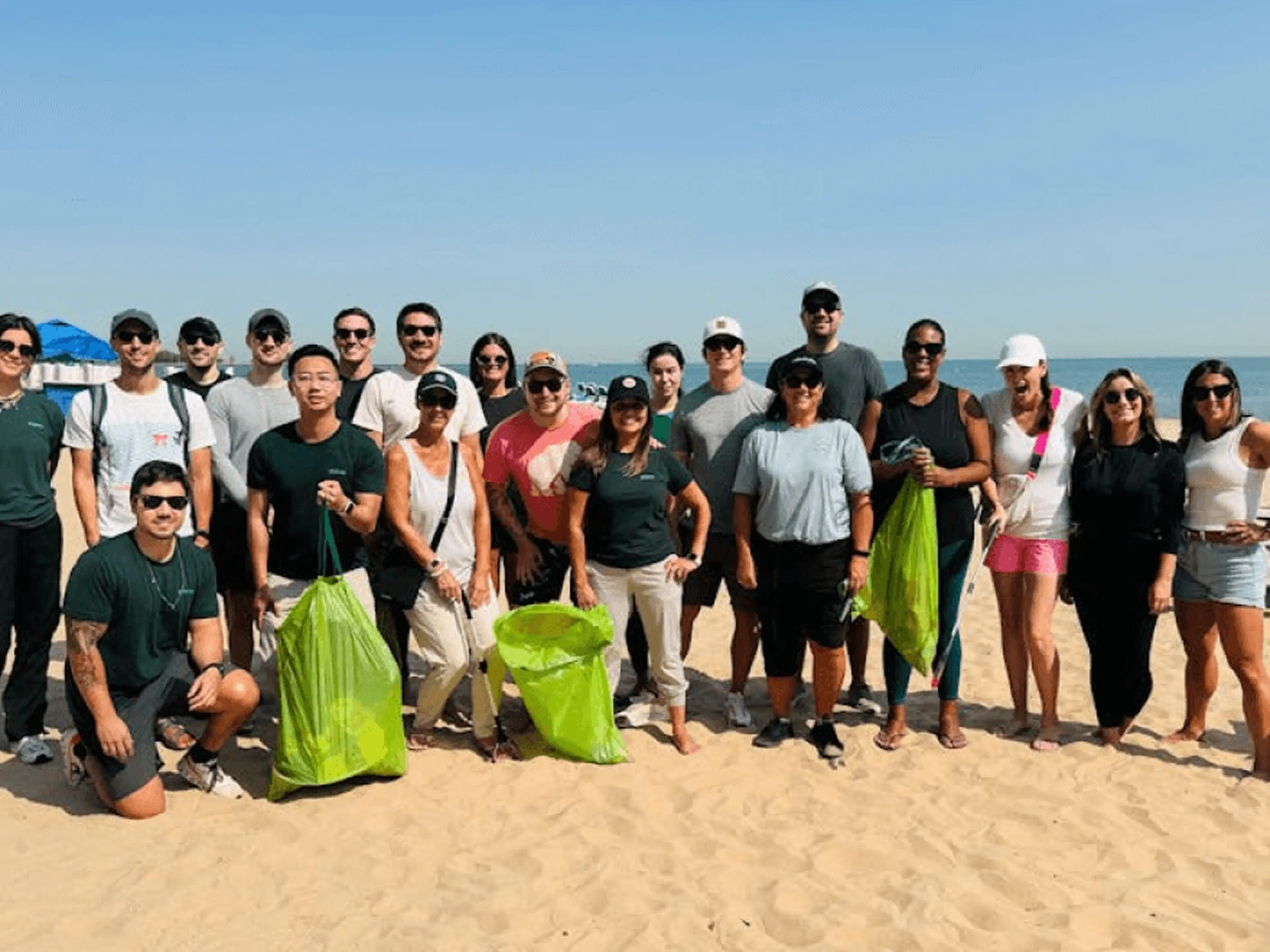 Volunteers on a sandy beach holding green and yellow trash bags during a cleanup.