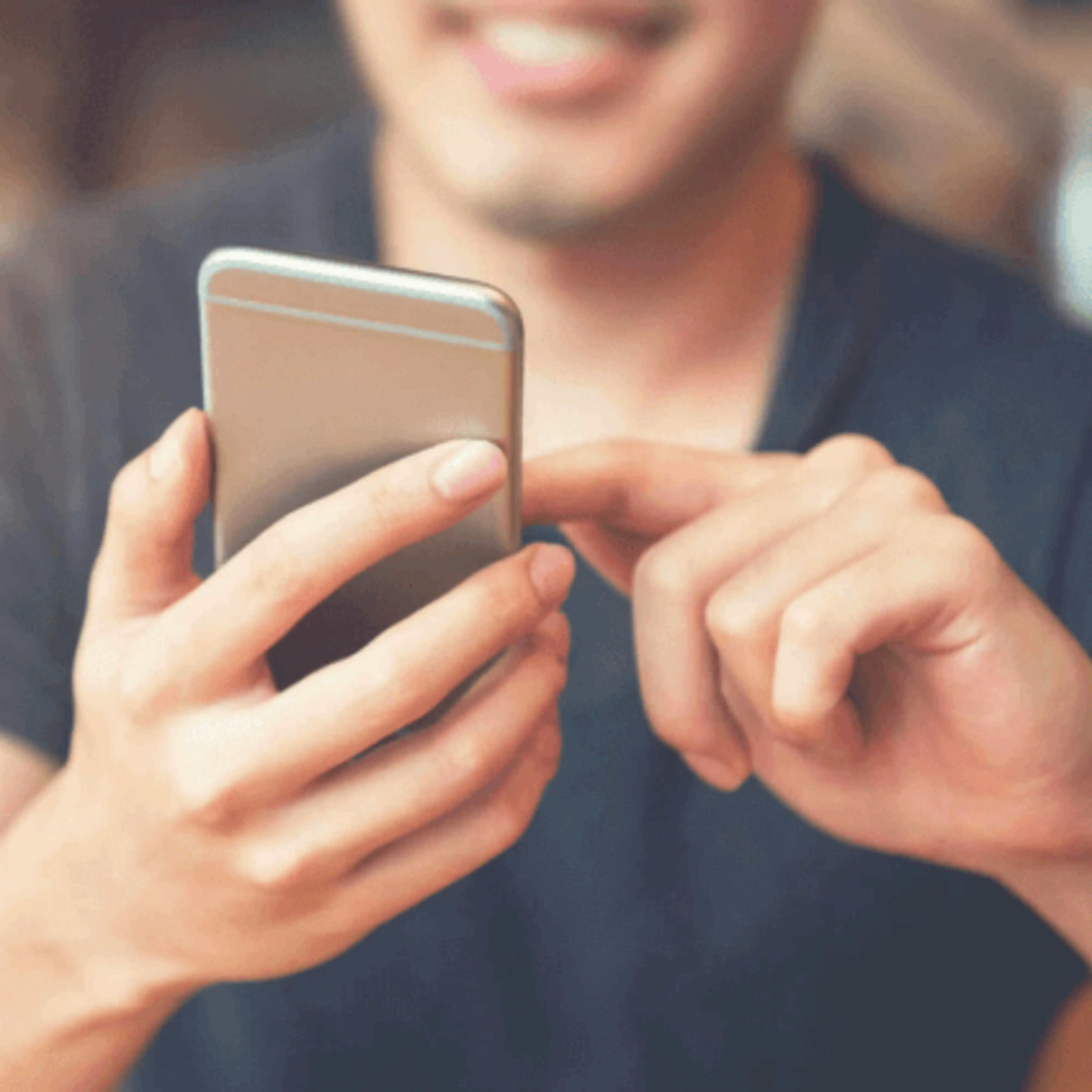 Man in gray shirt smiling while pressing buttons on his cellphone.