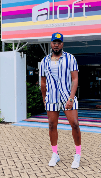 A man stands in front of an Aloft London hotel wearing a two piece blue striped outfit.