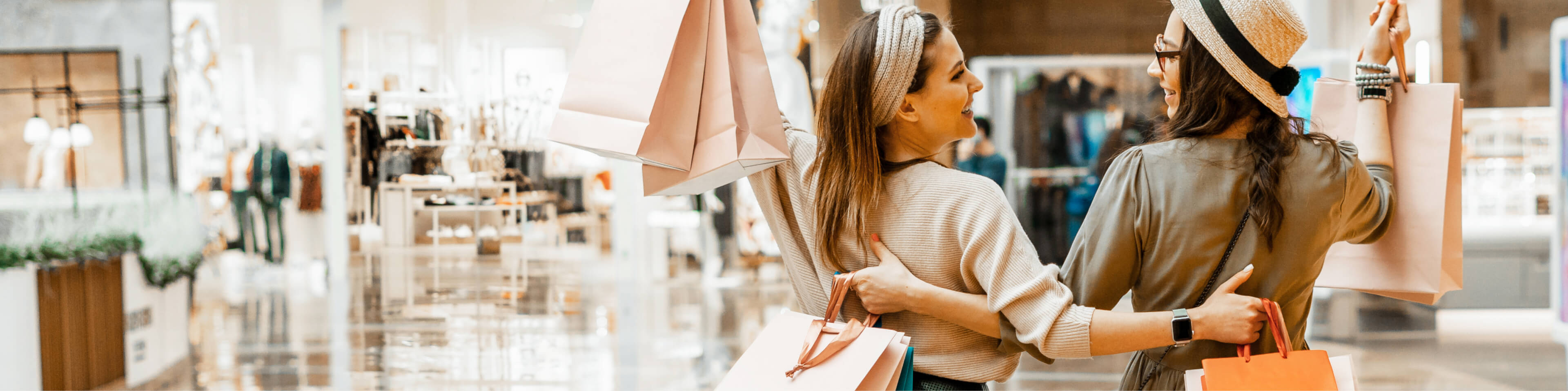 Two woman holding shopping bags in the mall looking at each other and smiling.