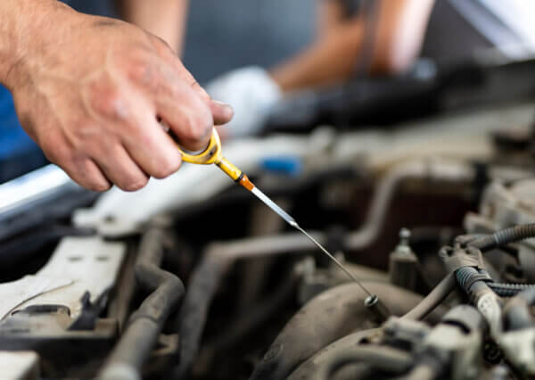 A car with the hood open is shown as someone changes the oil.