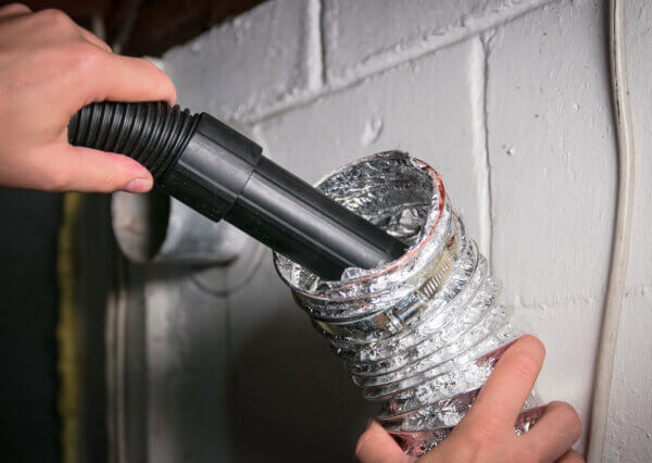 A closeup shot shows someone cleaning their own dryer vent, one of many popular home-related money saving hacks.