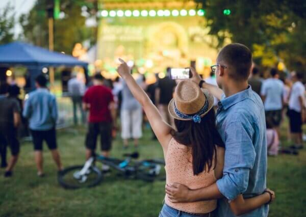 A couple is captured filming an outdoor stage at a festival.