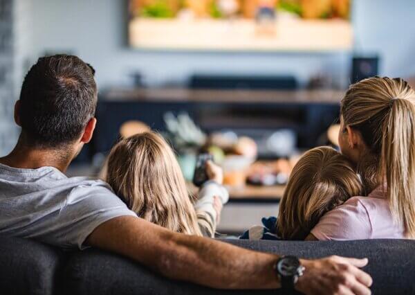 A father and his three children sit on the couch together while watching a movie. 