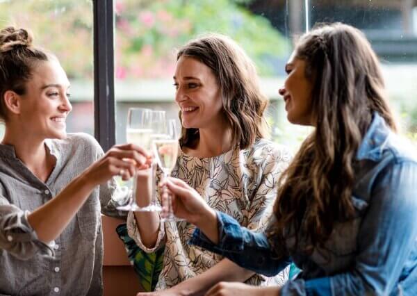 Three women each hold a glass of champagne as they share a toast.