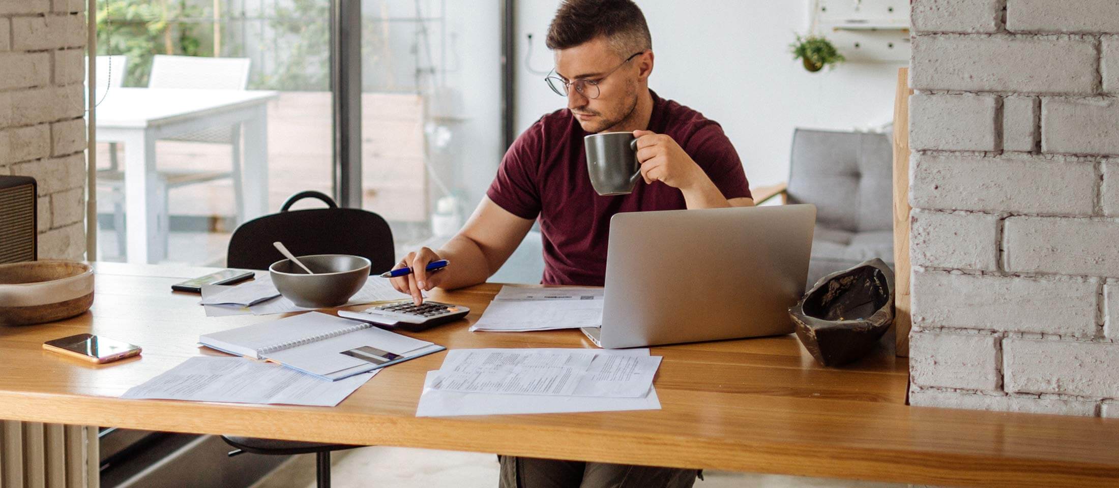 A person uses a calculator and holds a mug while researching how to set up direct deposit on their laptop.