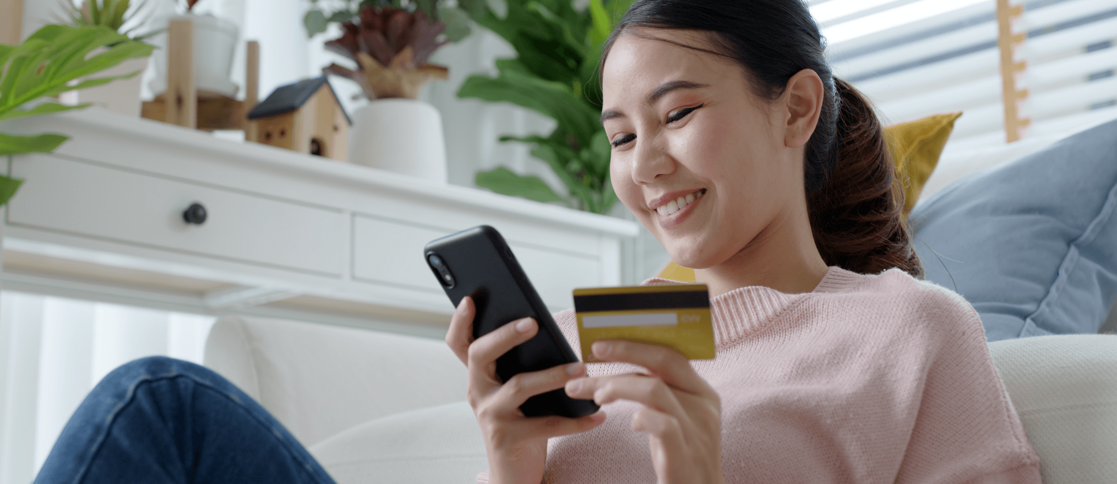 A young Asian woman holds a credit card while looking at her cell phone.