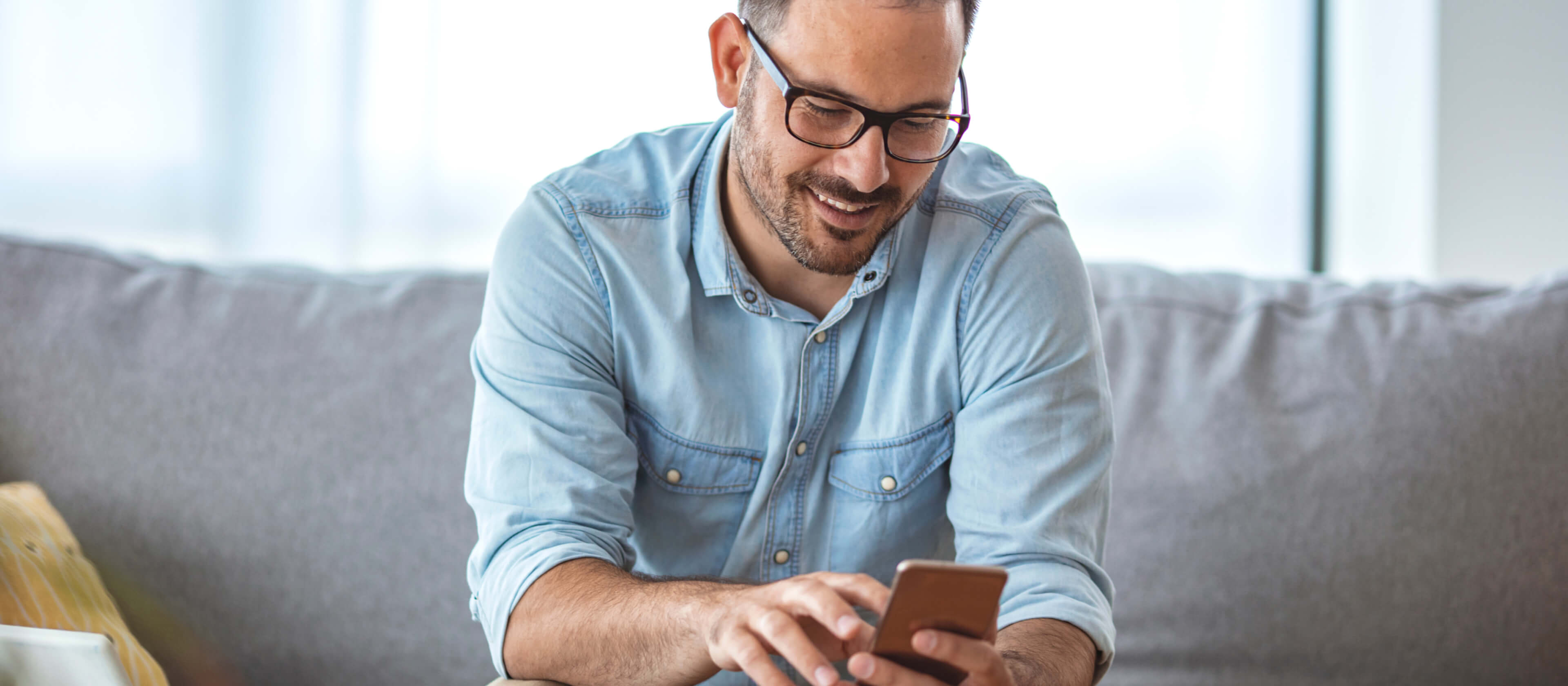 A man scrolls through his phone while smiling, presumably looking at his mobile banking app.